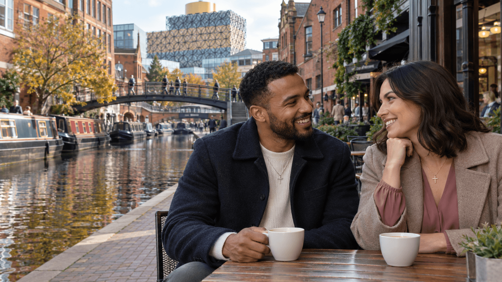 Couple wearing cross necklaces beside a canal in Birmingham, with the Library of Birmingham in the background.