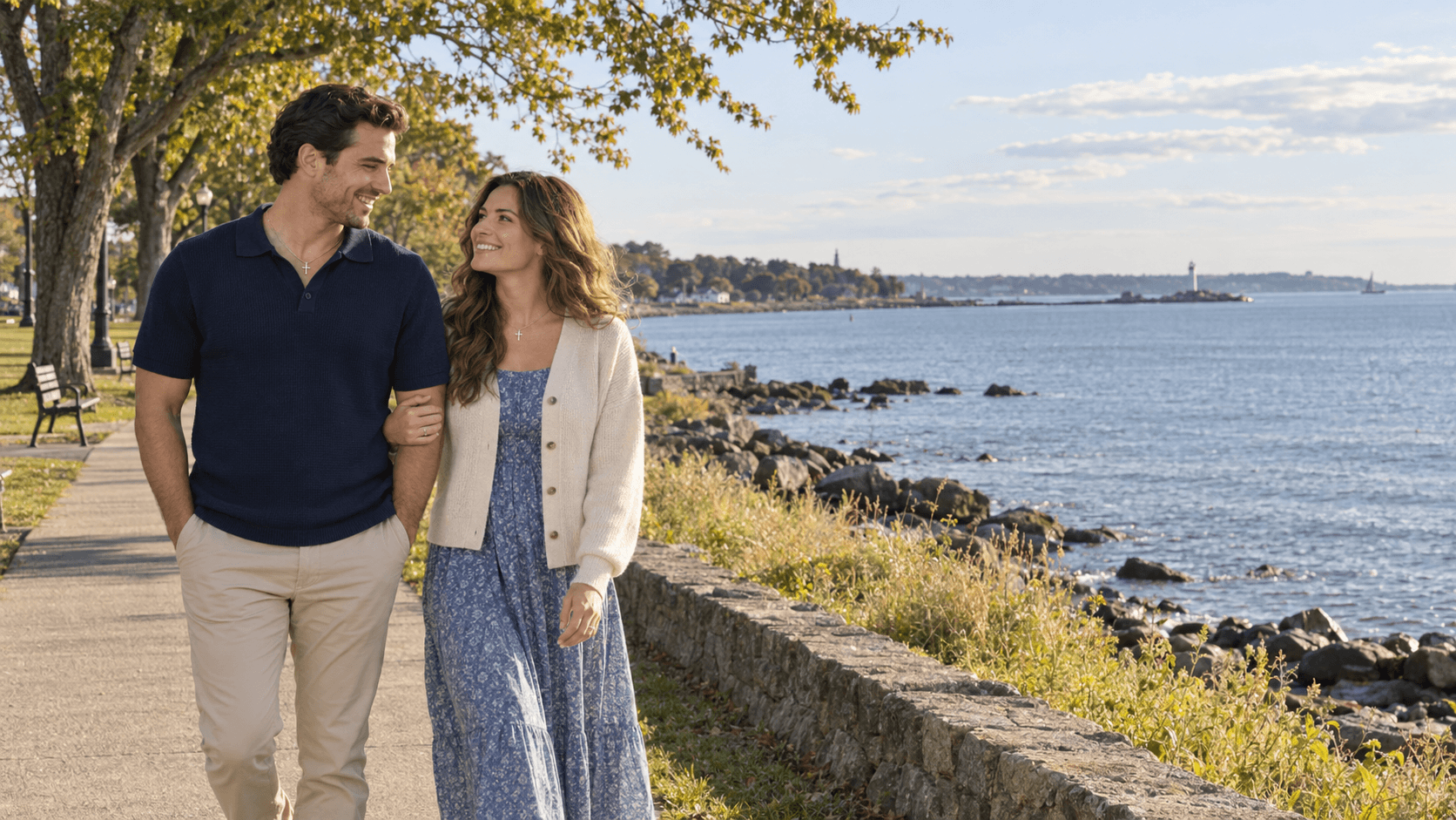 Couple wearing cross necklaces walking beside Long Island Sound in a Seaside Park-inspired scene.