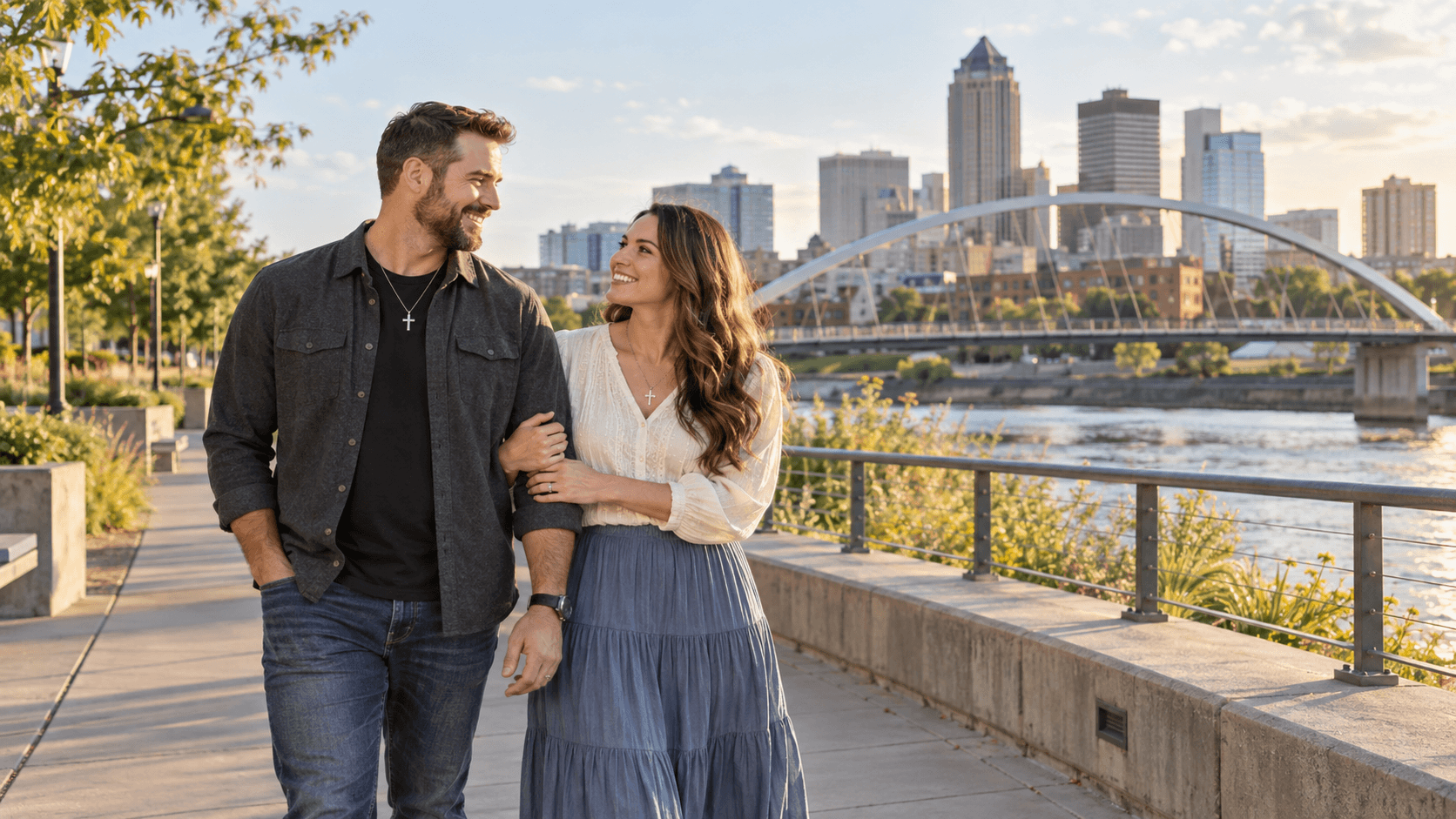 Couple wearing cross necklaces beside a Des Moines-inspired riverfront and downtown skyline.
