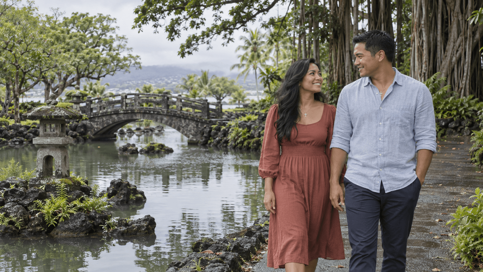 Couple wearing cross necklaces beside a pond and stone bridge in a Liliuokalani Gardens-inspired scene in Hilo.
