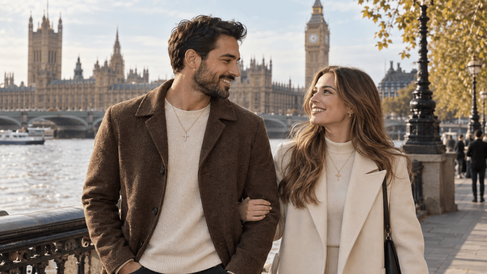 A couple wearing cross necklaces walking along the Thames in London, with the Houses of Parliament behind them